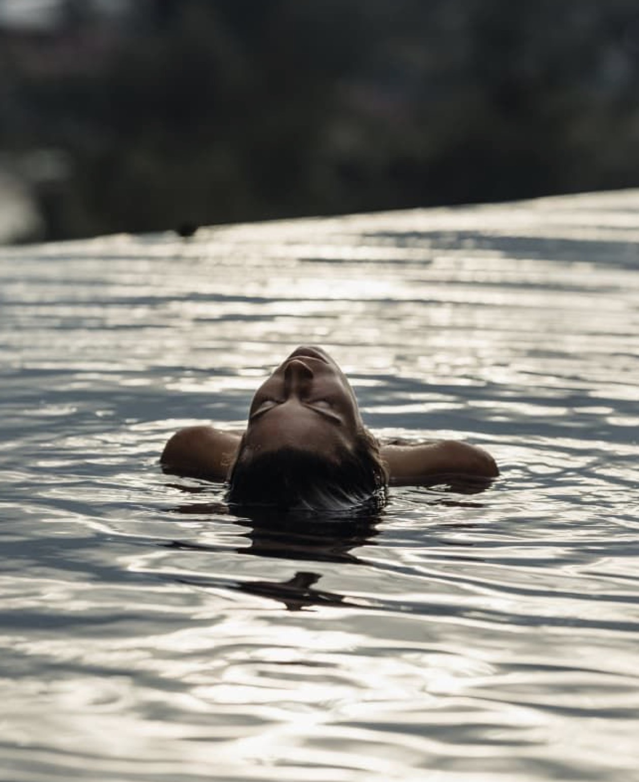A woman floating on her back in still water at dusk